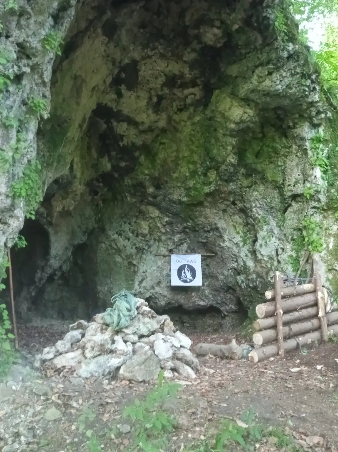 Ingresso di una grotta con bersaglio OUTLAWS e catasta di legna